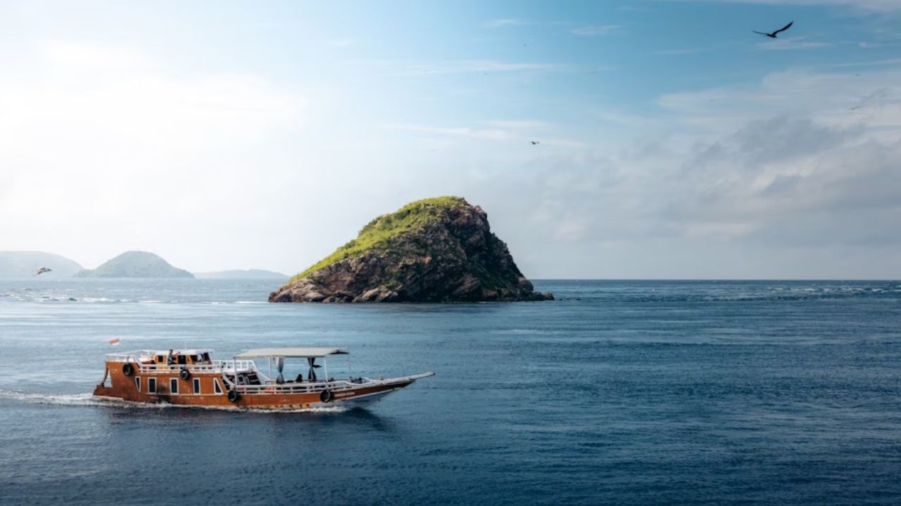 Wooden boat sailing near a small green island in clear blue waters.