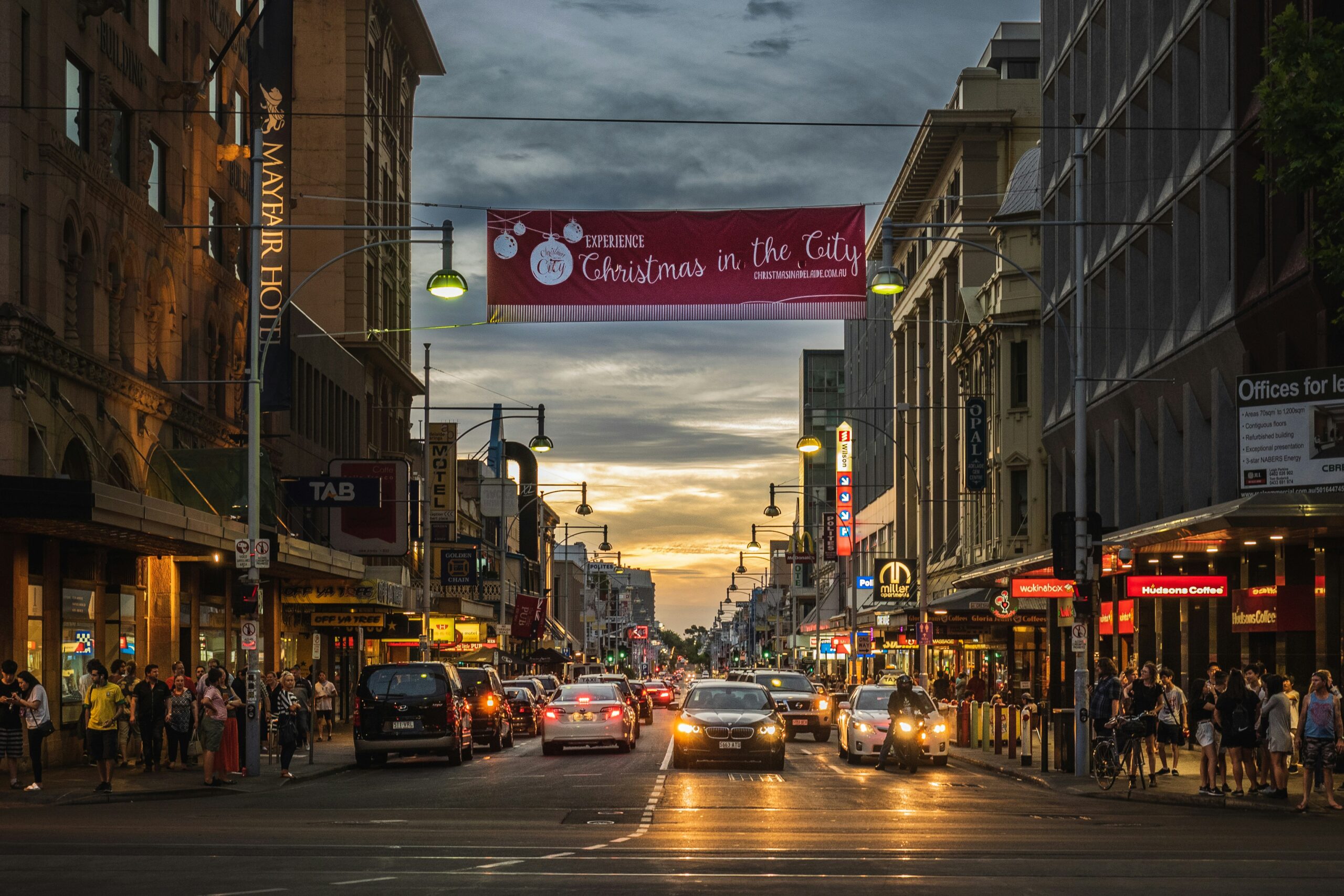 Cars and pedestrians crowd a city street at sunset beneath a "Christmas in the City" banner.