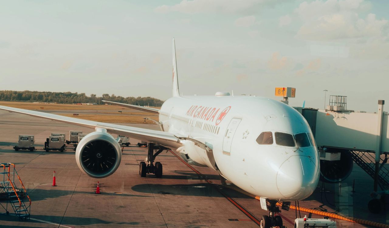 Air Canada plane at gate with boarding bridge and ground equipment.