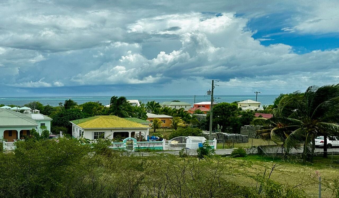 Colorful coastal homes in Antigua and Barbuda with ocean views under a dramatic cloudy sky