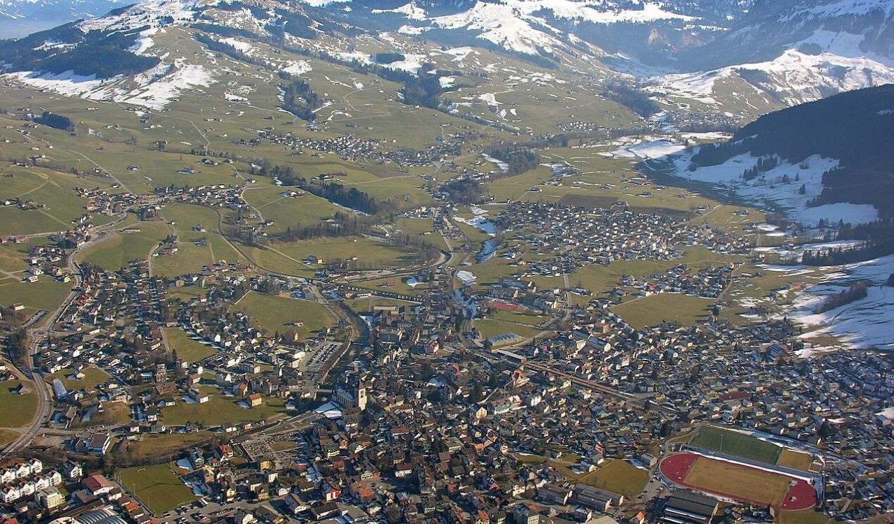 “Panoramic aerial view of Appenzell village nestled in green valleys below snow-capped Alpstein mountains, Switzerland