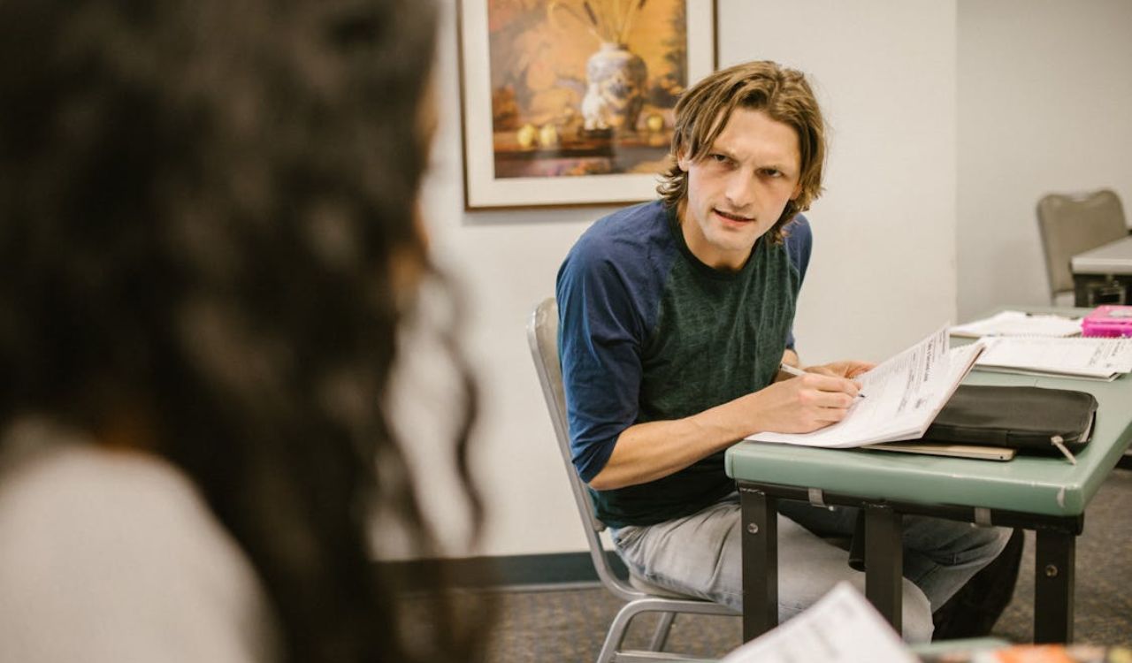 Man holding papers and speaking to a woman in a classroom setting
