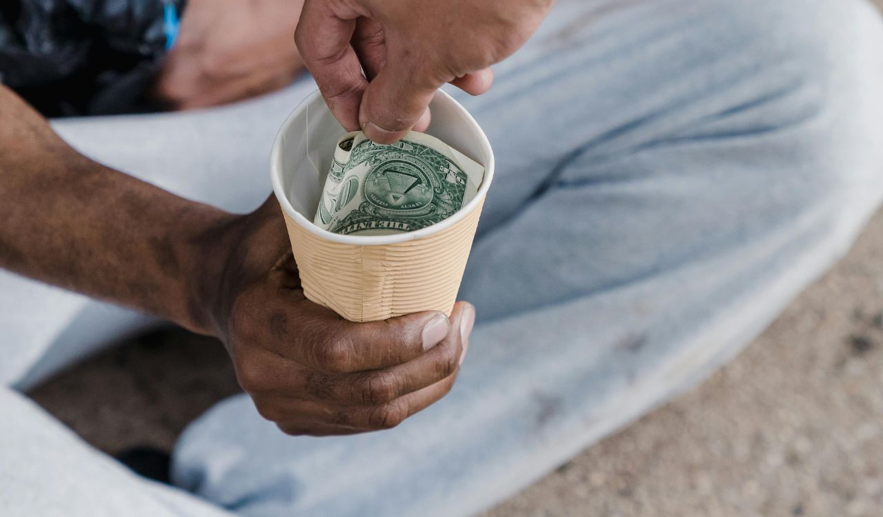 Hand putting money in a cup held by a person sitting.