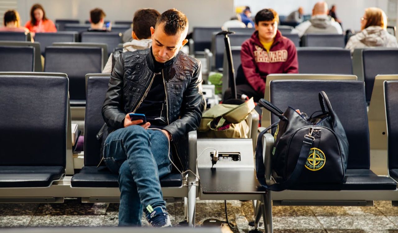 Man using phone near public charging station at airport.