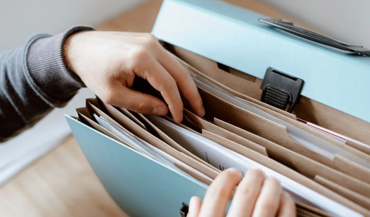Hands organizing papers in a blue document folder.