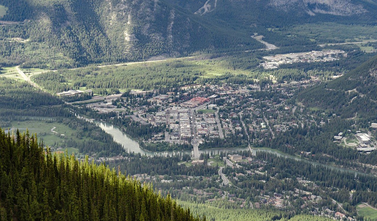Aerial view of Banff town nestled in a lush valley, surrounded by dense forests and tall mountains