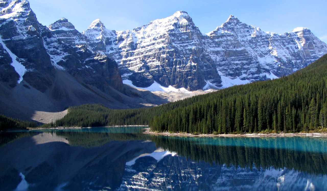 Snowy mountains reflected in a turquoise lake, surrounded by pine forest.