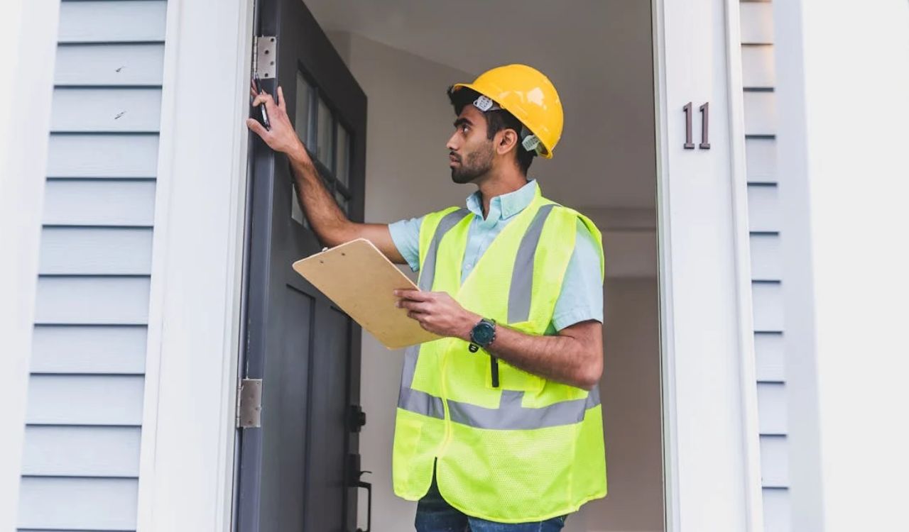 Home inspector in safety vest and hard hat examining a front door with a clipboard