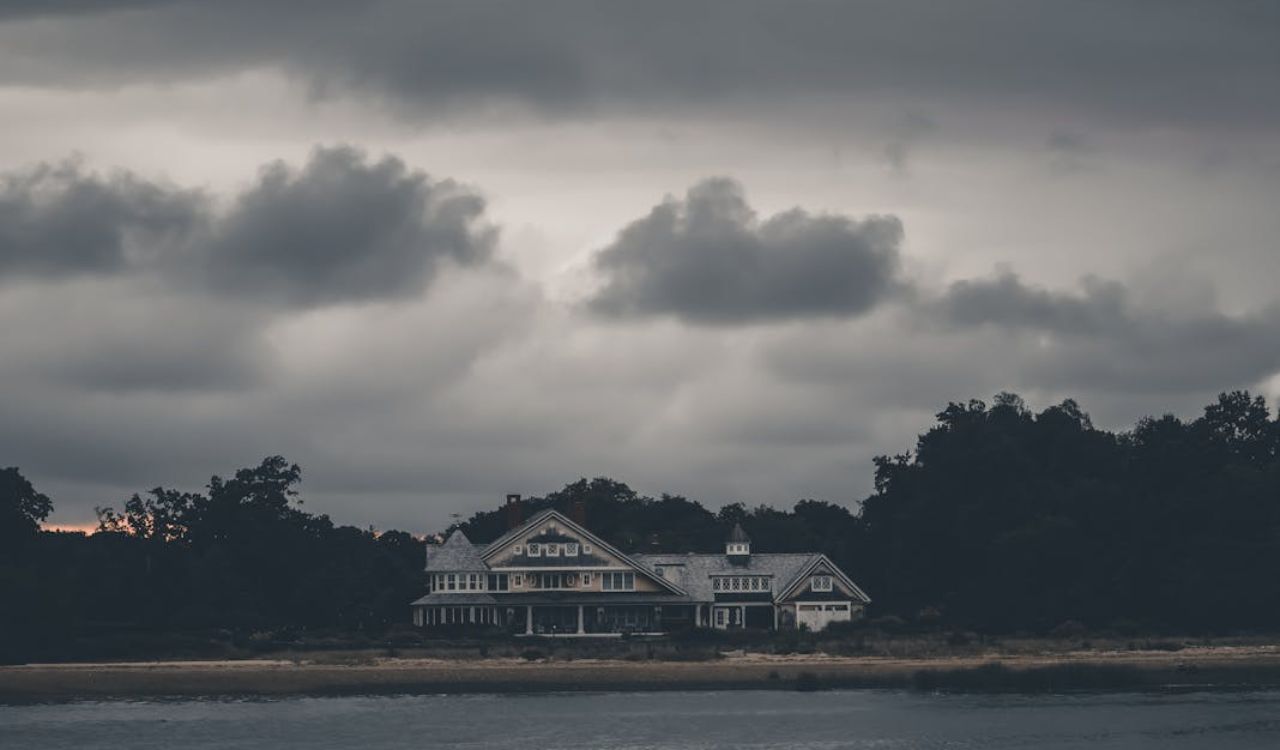 Large beachfront house under dark, stormy skies, suggesting potential real estate risks