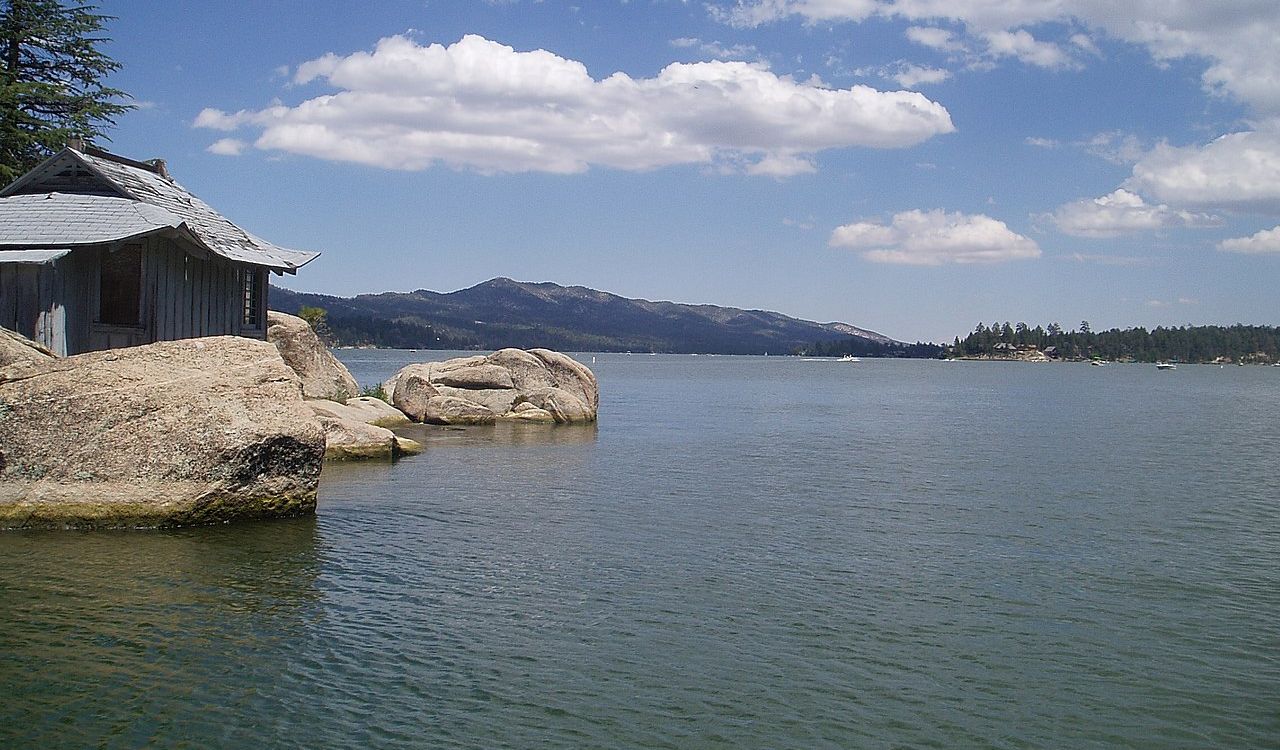 Rustic lakeside cabin on rocks with mountain views under a blue sky