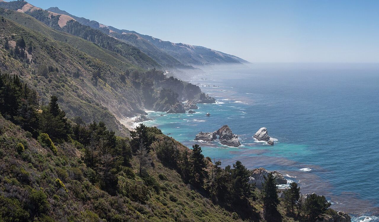 Big Sur's dramatic cliffs meet the endless Pacific, where mist rises over rugged shores and turquoise waters crash below pine-covered slopes