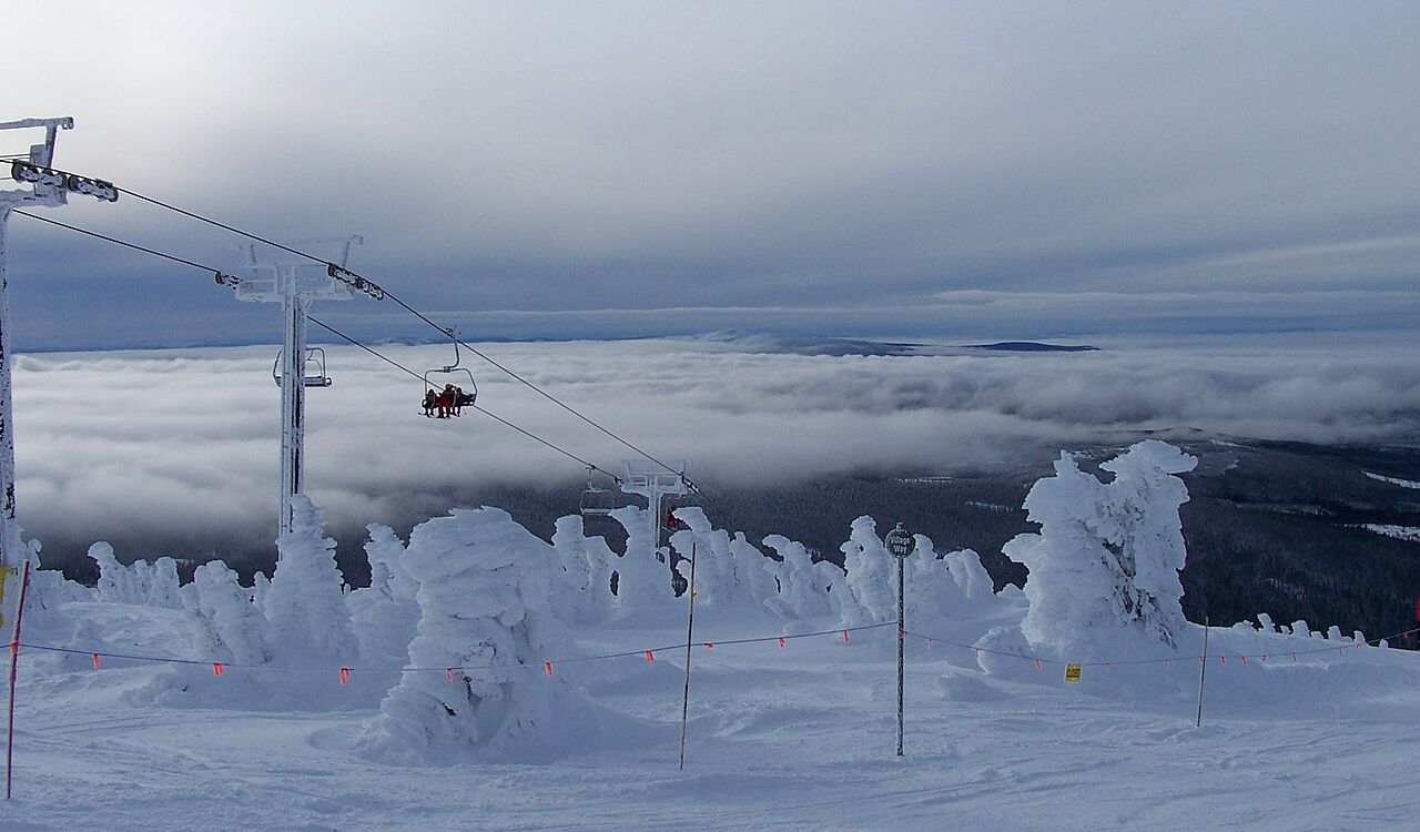 Snow-covered trees and a ski lift rise above the clouds at Big White, British Columbia