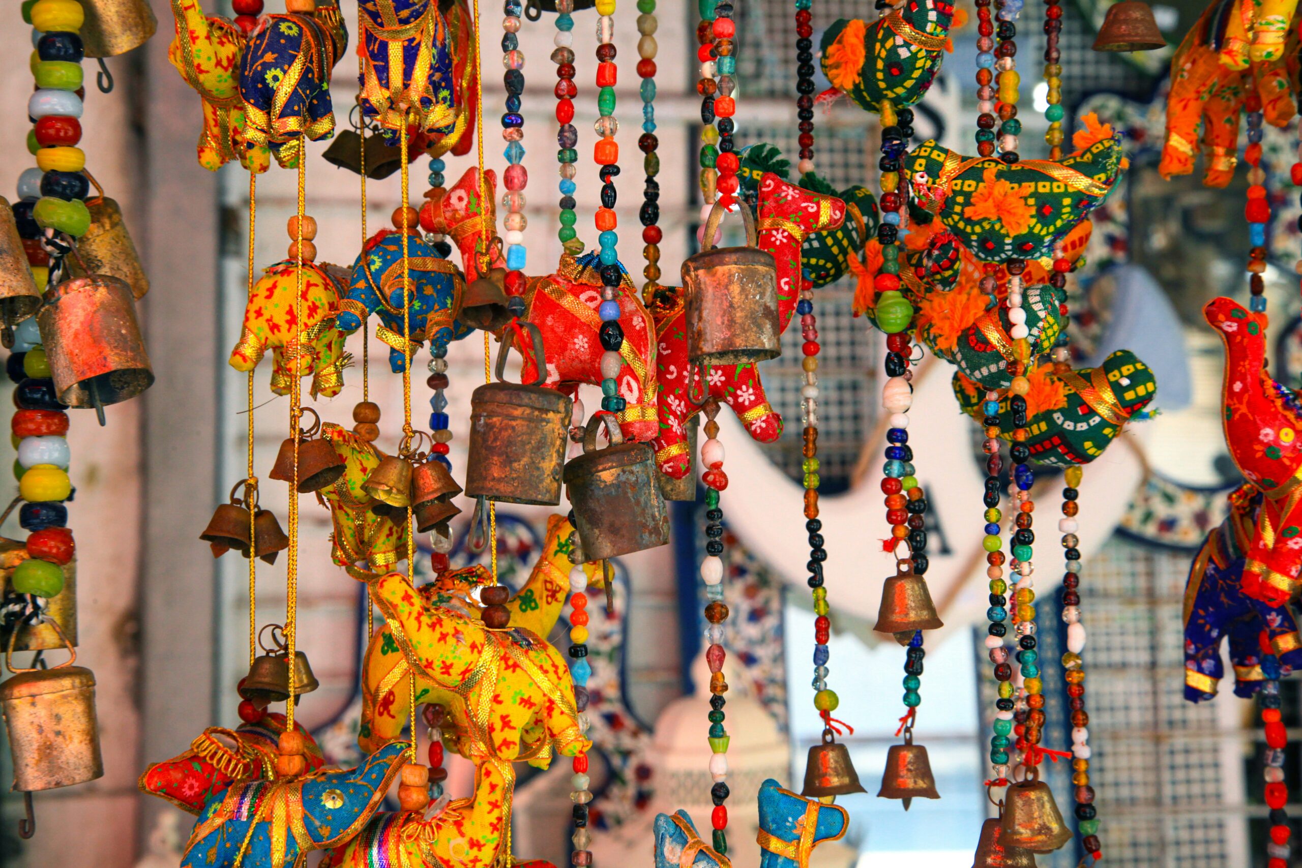 Colorful hanging decorations of beads, bells, and painted animal shapes are displayed in a market or shop.
