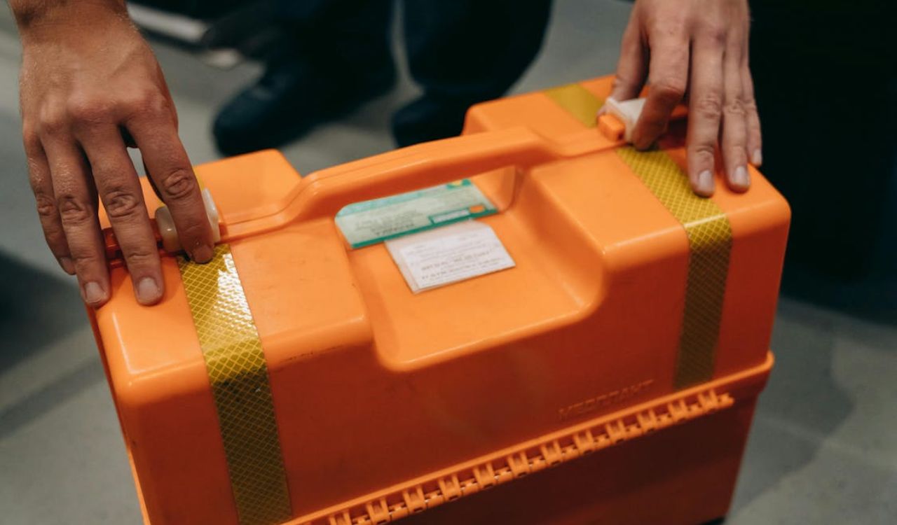 Hands holding an orange first-aid kit box with labels on top