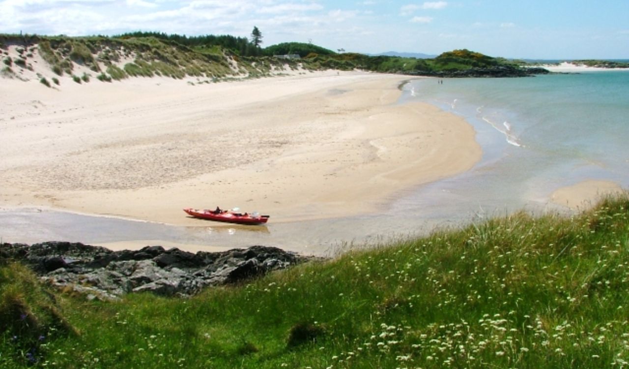 A red kayak rests on the sandy shore of Camusdarach Beach
