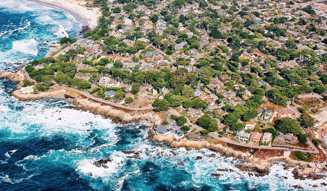 A charming coastal town hugs the rugged shoreline, where waves crash below rows of cozy homes nestled in lush greenery