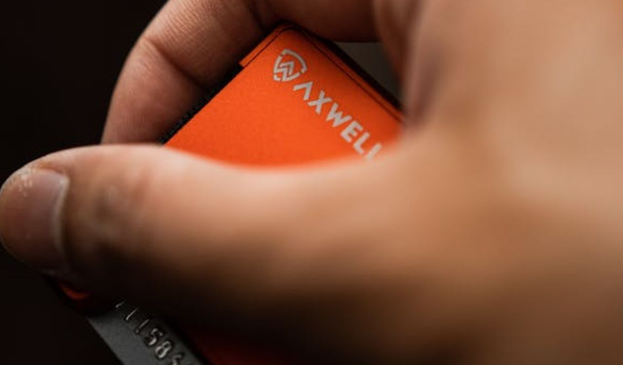 Close-up of a hand holding an orange AXWELL wallet.