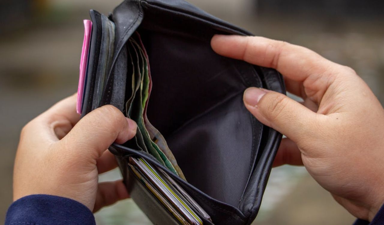 Hands holding an open, mostly empty black wallet.