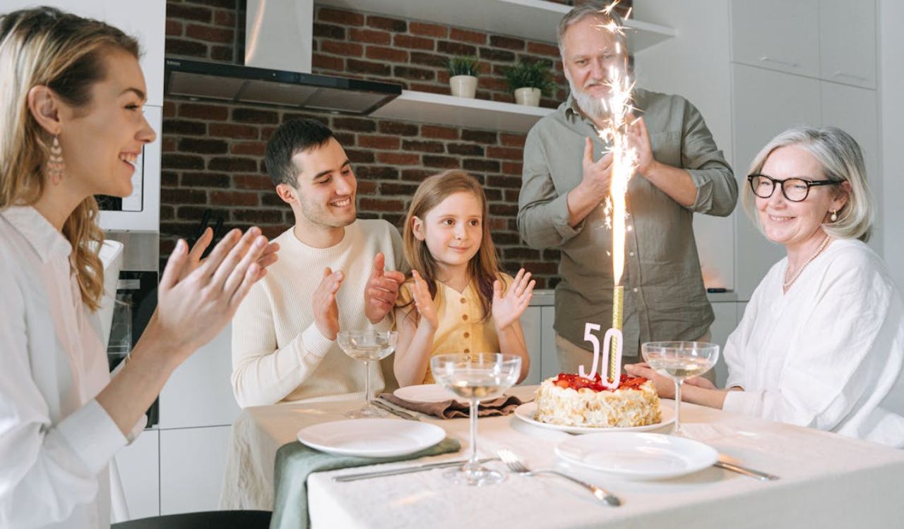 Family celebrating a 50th birthday with cake and sparklers in a cozy kitchen setting
