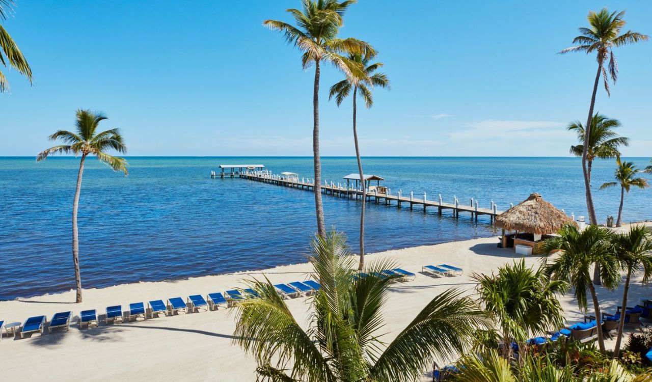 Beachfront view at Cheeca Lodge & Spa in Islamorada with palm trees, lounge chairs, and a long wooden pier stretching into calm blue waters