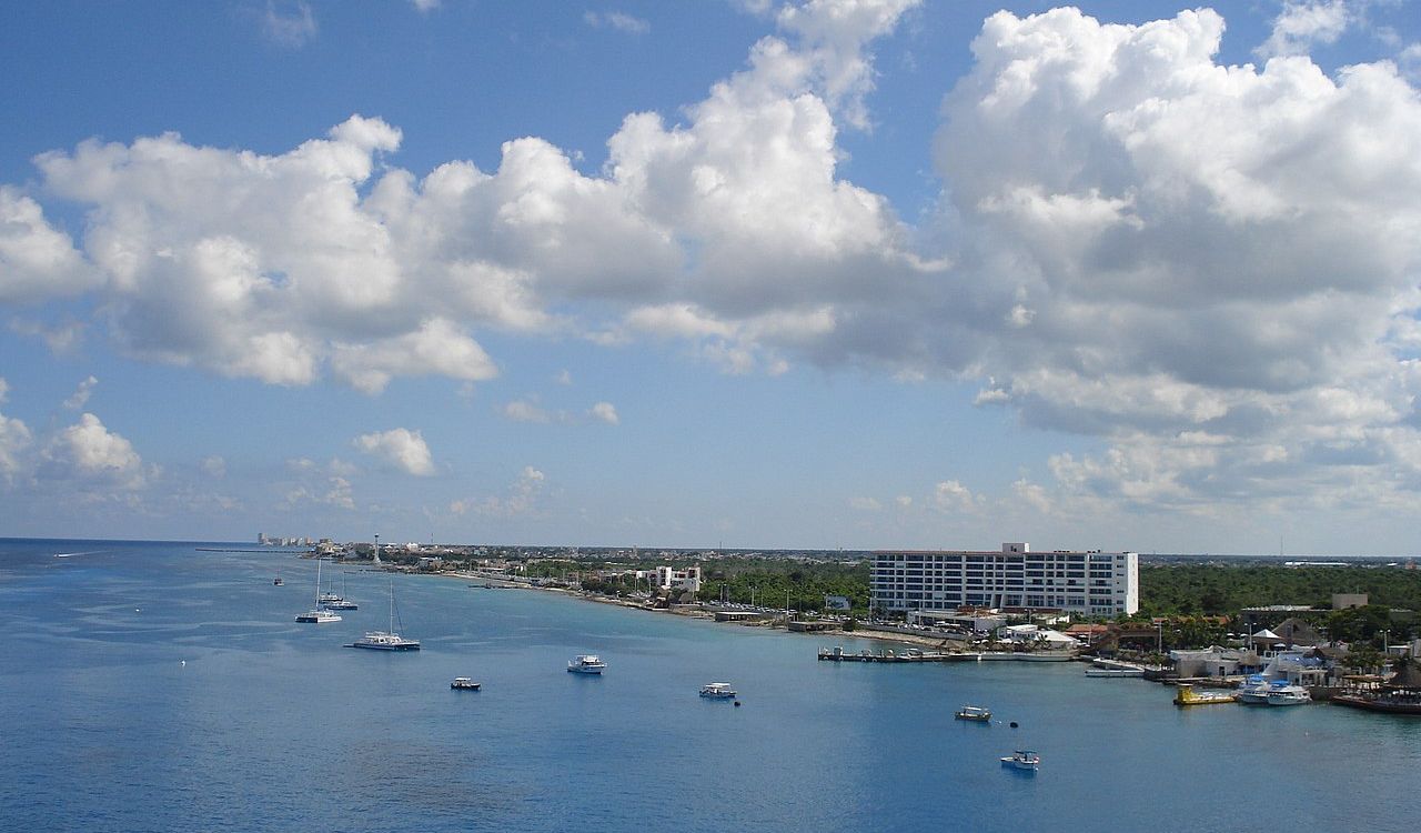 Cozumel coastline with calm blue water, boats, and a few coastal buildings