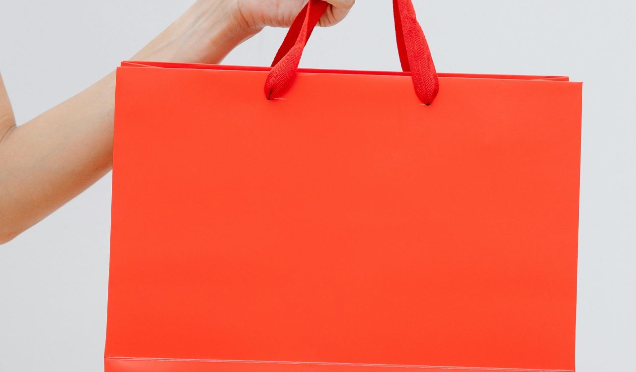 Hand holding a bright red shopping bag.