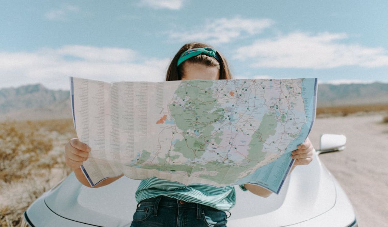 Woman reading a map while leaning on a car in a desert landscape