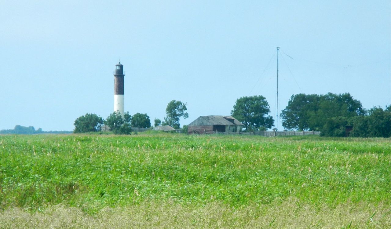 Striped lighthouse and rustic farmsteads amid windswept grasslands on Hiiumaa Island, Estonian archipelago