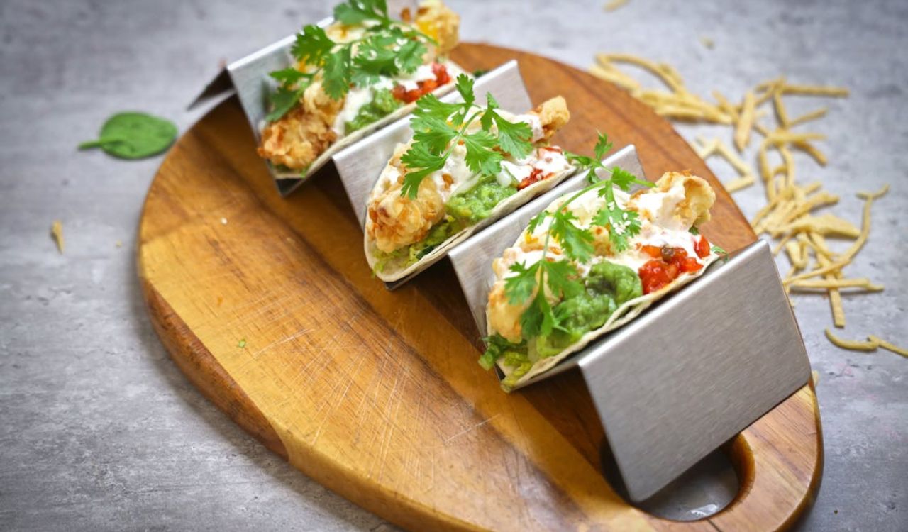 Three loaded tacos with guacamole, salsa, and cilantro served on a wooden board