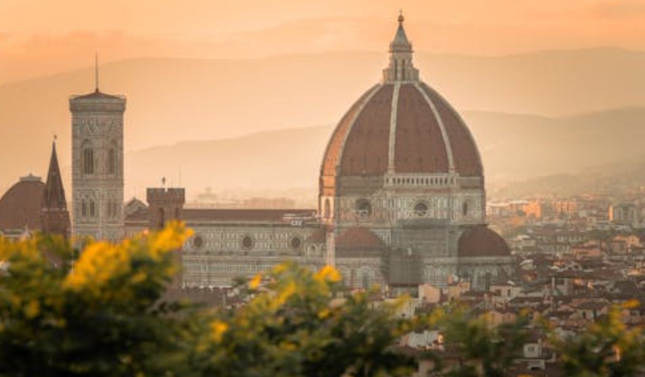 View of the Florence Cathedral (Duomo di Firenze) during sunset, with its iconic dome and bell tower towering over the city skyline