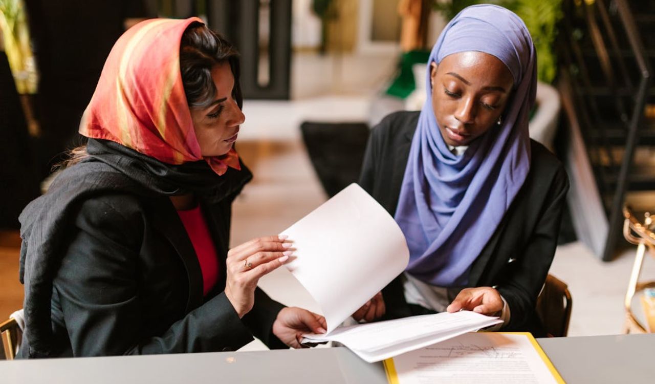 Two women in hijabs reviewing travel documents together at a table