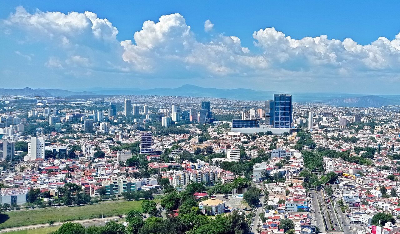 Modern skyline of Guadalajara, Mexico, with mountains in the distance under a bright blue sky