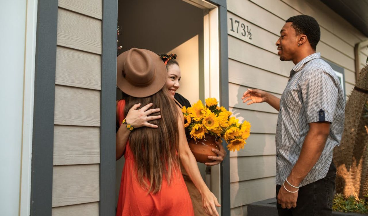A woman greeting guests at her front door, holding a pot of sunflowers with a warm smile