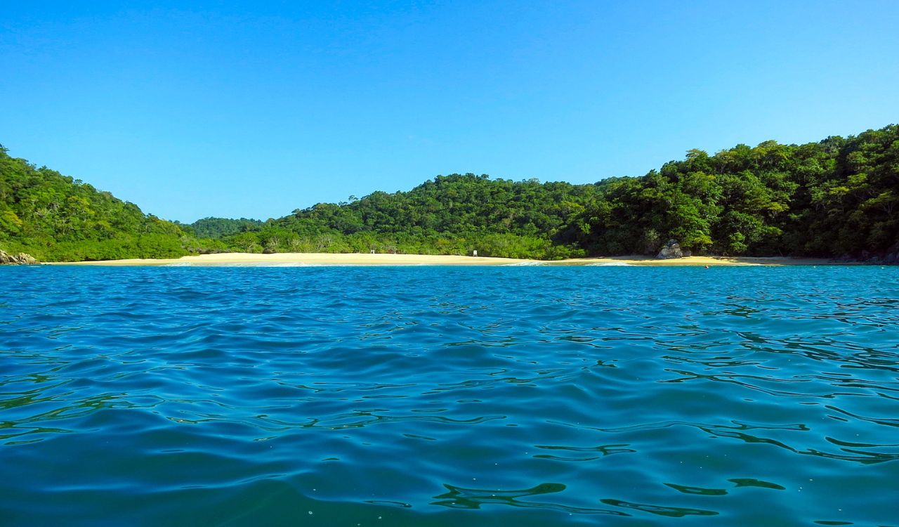 Clear blue water with a quiet beach and green hills in Huatulco, Mexico