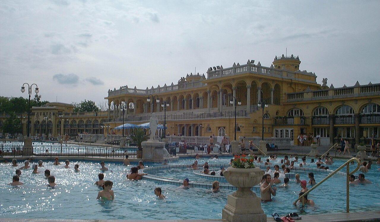 Széchenyi Thermal Bath in Budapest, Hungary, with people relaxing in large outdoor pools surrounded by grand Neo-Baroque architecture