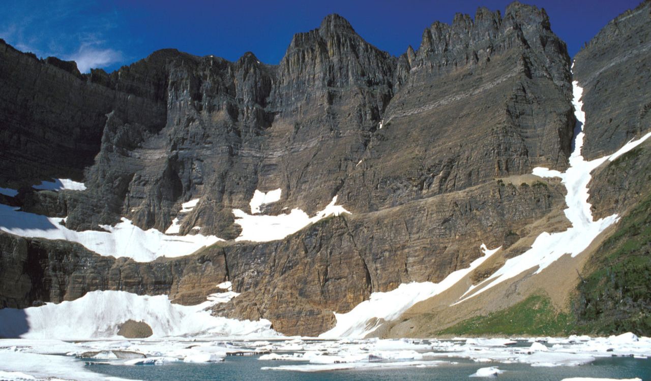 Steep rocky cliffs and floating ice chunks on Iceberg Lake in Glacier National Park, Montana