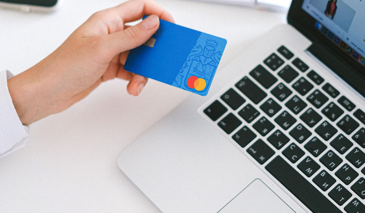Hand holding a credit card near a laptop keyboard.