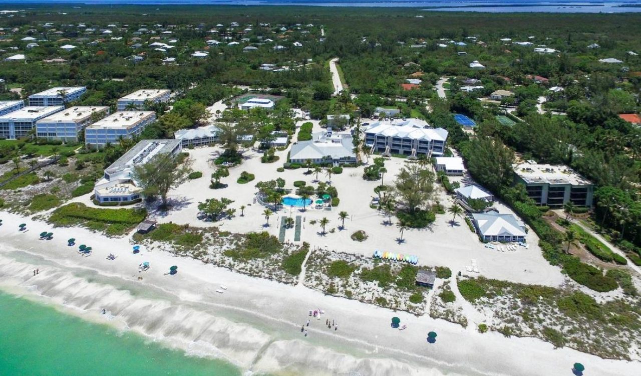 Aerial view of Island Inn on Sanibel Island, with beachfront accommodations, a central pool, and umbrellas lining the shore