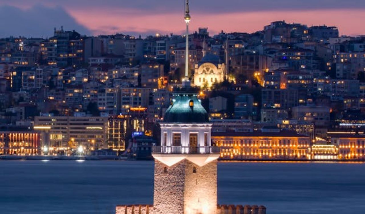 A scenic view of the Maiden's Tower illuminated at night with a city skyline in the background