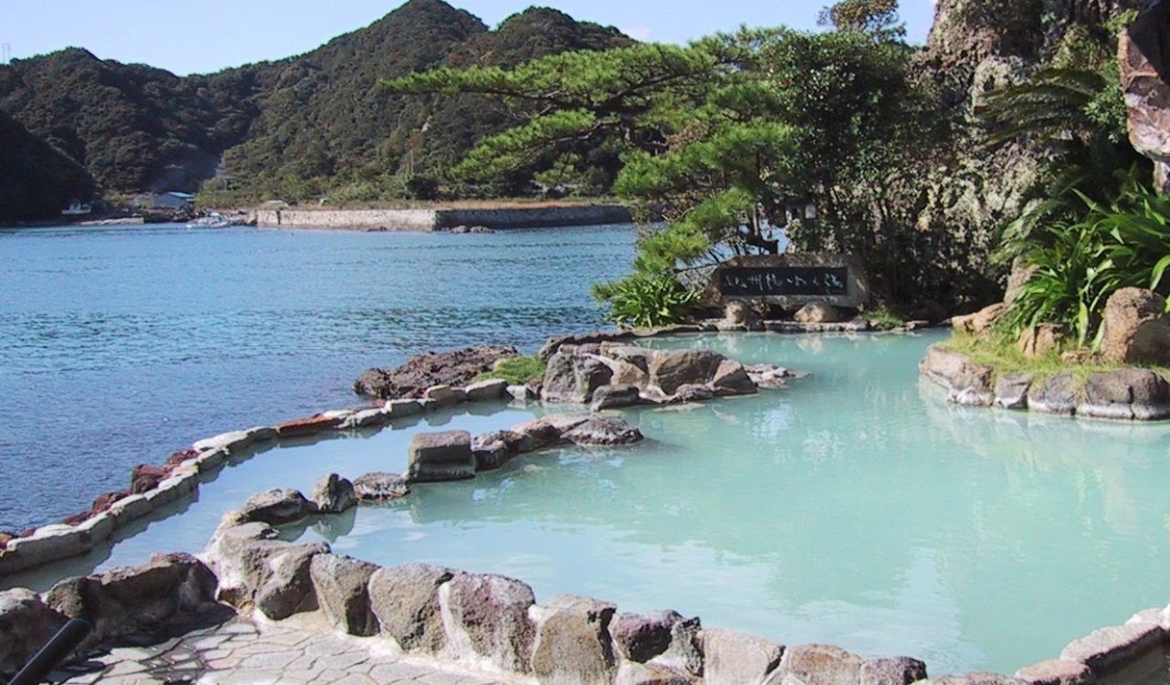 Scenic Japanese onsen by the sea surrounded by rocks and lush greenery