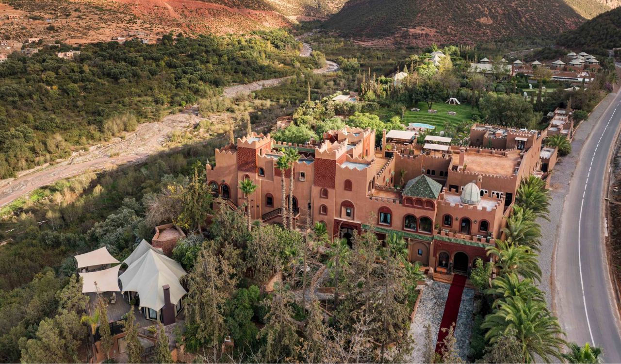 Kasbah Tamadot, a luxury Moroccan-style hotel nestled in the Atlas Mountains, surrounded by lush greenery and red hills