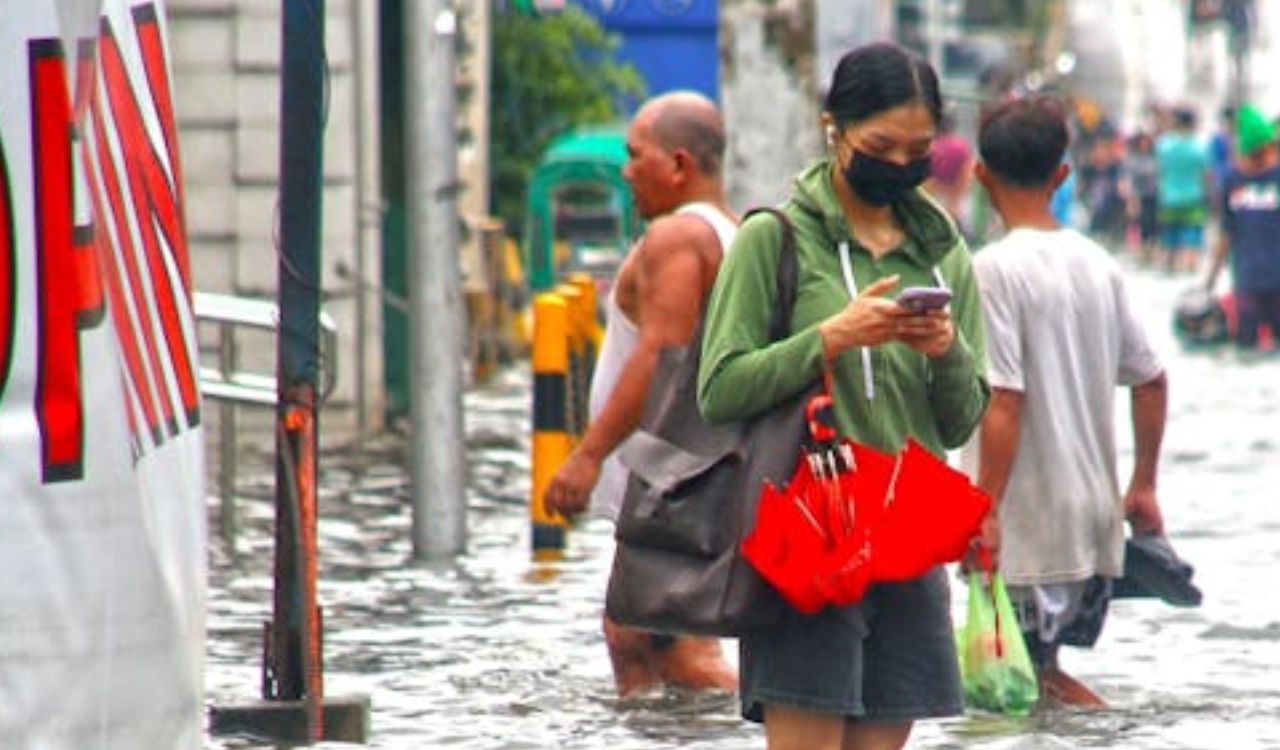 People walking through a flooded street; woman in front checking phone.