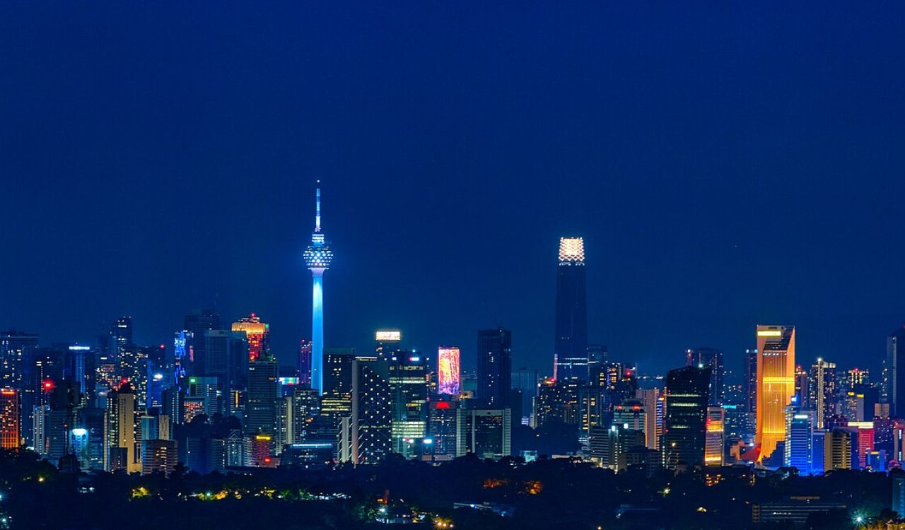 A stunning night view of Kuala Lumpur's skyline, featuring the iconic Petronas Twin Towers, Menara KL Tower, and modern high-rise buildings illuminated with vibrant city lights