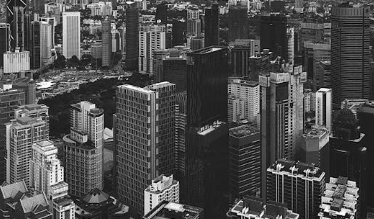 Black-and-white aerial view of Kuala Lumpur’s modern skyline beneath dramatic storm clouds