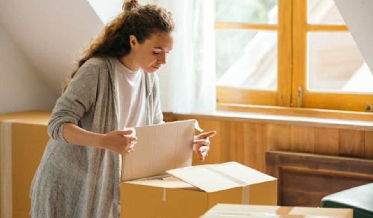 Woman opening a cardboard box in a sunlit room with several packed boxes