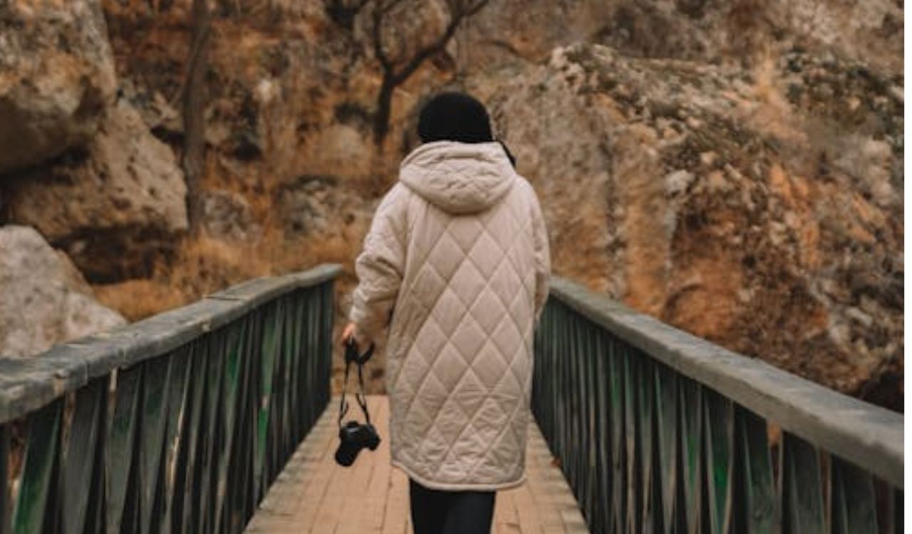 Person walking alone on a bridge in a rocky landscape wearing a quilted coat