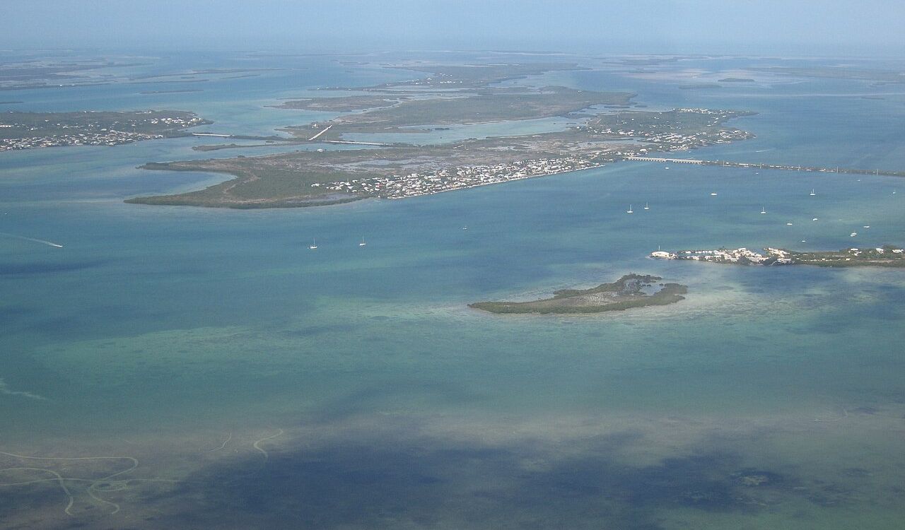 Aerial view of Little Palm Island and surrounding keys in Florida, featuring clear blue waters, small boats, and scattered buildings.