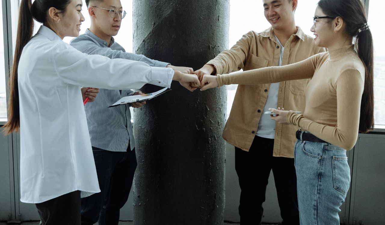 Four people in an office giving friendly fist bumps, showing teamwork and collaboration.