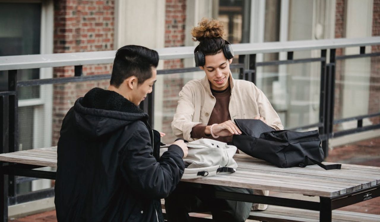 Two friends chat while unpacking backpacks outside.