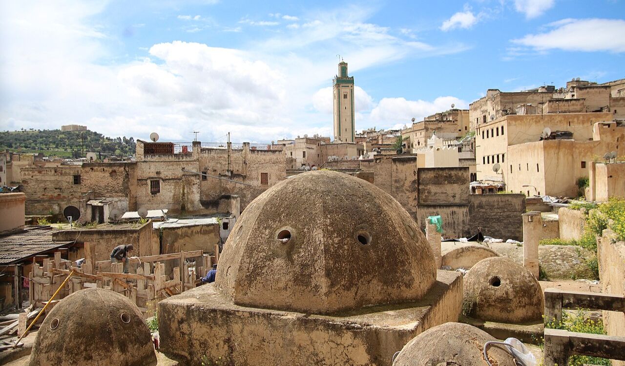 Traditional hammam domes in the old medina of Fez, Morocco, with ancient stone architecture and a tall minaret in the background